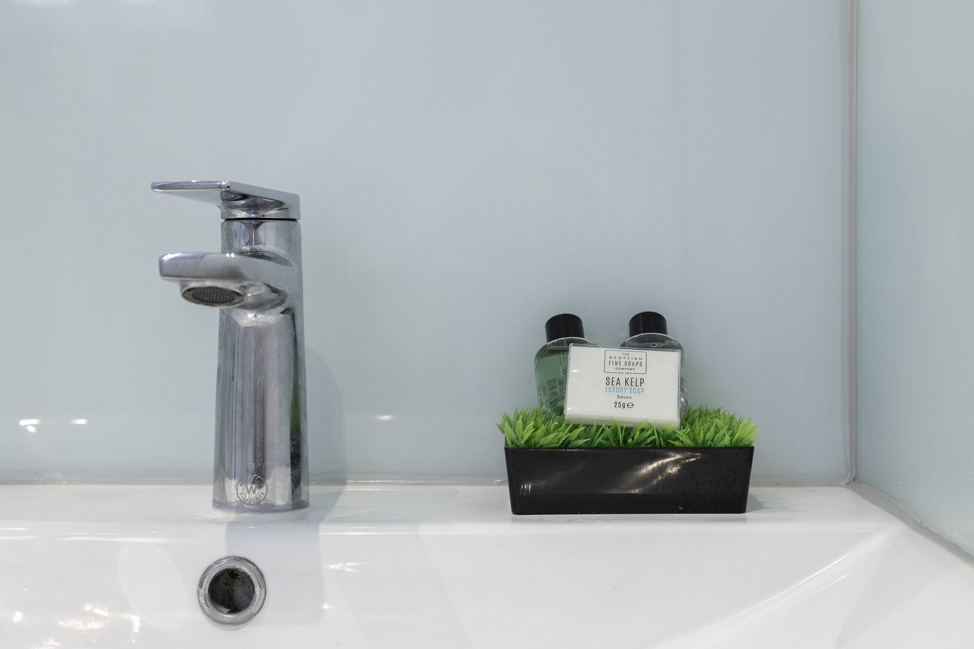 A bathroom sink with a chrome faucet and a black soap dispenser with two bottles.