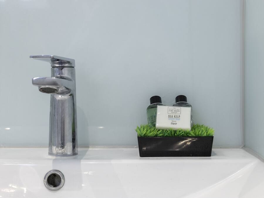 A bathroom sink with a chrome faucet and a black soap dispenser with two bottles.