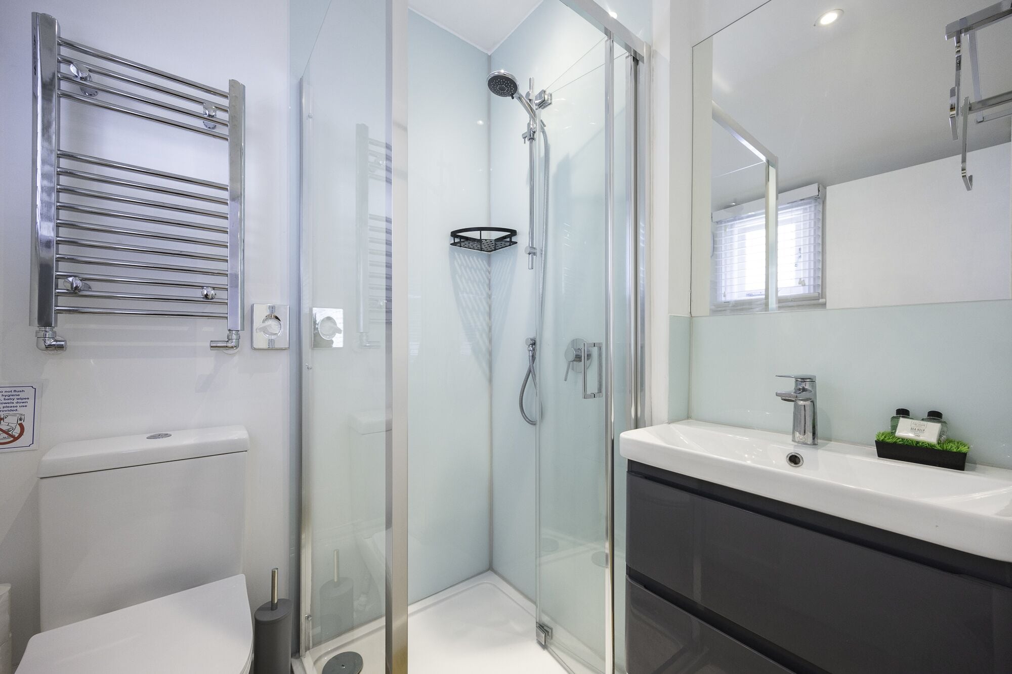 Un bany modern amb dutxa envidriada, un lavabo blanc i un suport per a tovalloles.