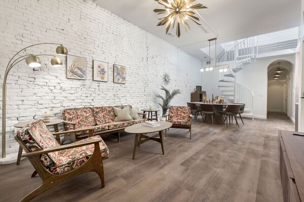 A modern living room with a white brick wall, wooden flooring, and a staircase leading to an upper level.