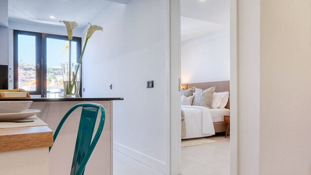 A modern hotel room with a bed, a bedside table, and a view of the cityscape through large windows. - Beco Santa Emilia 4P, a Home in Madeira (Funchal)