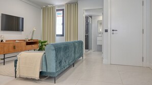 A modern hotel room with a sofa, a wooden console table, a TV, and a bathroom visible through a glass door. - Beco Santa Emilia 4P, a Home in Madeira (Funchal)