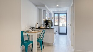 A modern kitchen with a dining area, white walls, and a view of a cityscape through a glass door. - Beco Santa Emilia 4P, a Home in Madeira (Funchal)