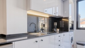 A modern kitchen with white cabinets, a stainless steel sink, a built-in oven, and a washing machine. - Beco Santa Emilia 4P, a Home in Madeira (Funchal)