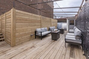 Eine Terrasse im Freien mit Holzboden, einer Couch, einem Sessel und einem kleinen Tisch.