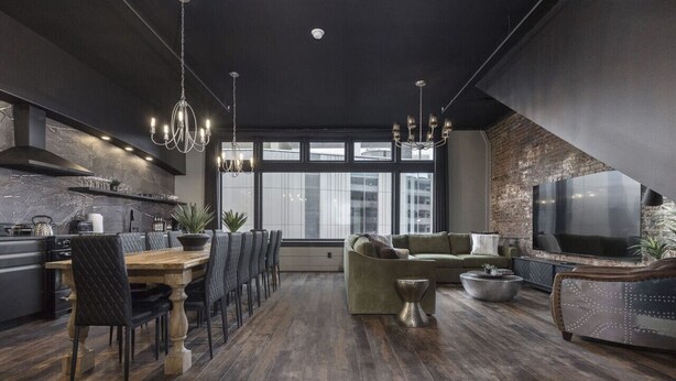 A modern kitchen with a dining area, a living room with a sofa and TV, and a large window providing natural light. - Penthouse Grand Executive Suite (Louisville)