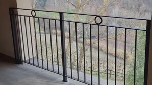Un balcon doté d’une rambarde en métal, d’un sol en béton et offrant une vue sur une zone boisée où les arbres sont sans feuilles.