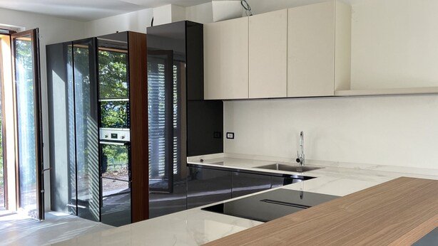 Une cuisine moderne dotée d’un plan de travail en bois, de meubles blancs et d’une porte en verre donnant sur un espace extérieur.