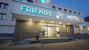 Een modern hotel met een opvallend bord 'FRIENDS HOTEL', een logo met 'fh' en een cirkelontwerp, en een trap die naar de ingang leidt.