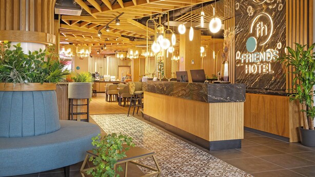 Een hotel receptie met een houten balie, zitplaatsen en een decoratieve wand met de naam van het hotel.
