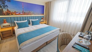 Een hotelkamer met een bed, bureau, stoel, nachtkastje, lamp, schilderij van een stadsgezicht en een raam met gordijnen.