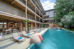 Um hotel com área de piscina, cadeiras de descanso e um elemento aquático.