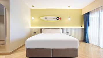Una moderna camera d'hotel con un ampio letto, un surf adornato al muro e vista sull'oceano dalla finestra.
