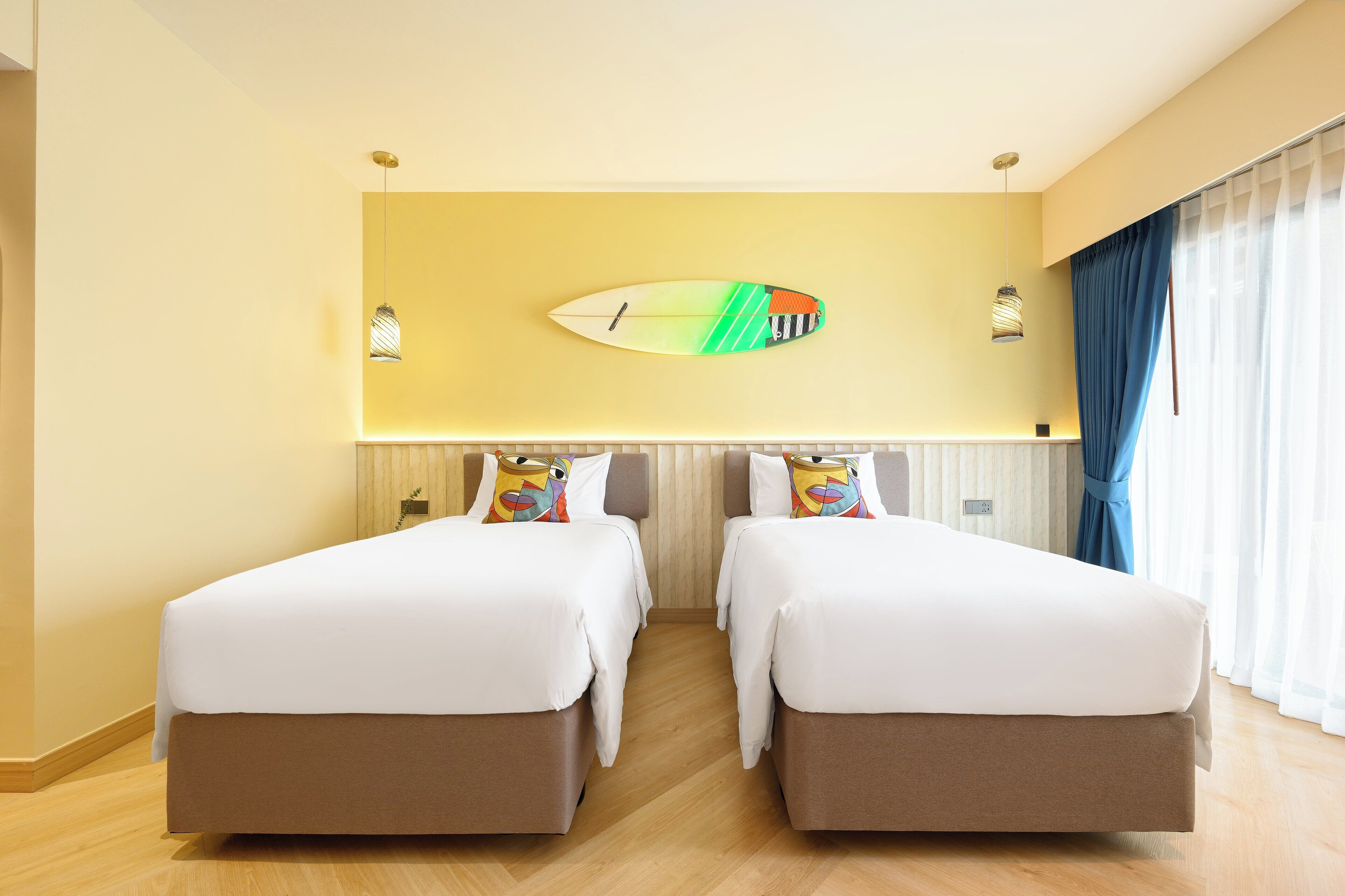 Habitación de hotel con dos camas, un adorno de tabla de surf en la pared y una ventana con cortinas.