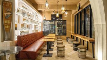 Un acogedor interior de cafetería con un asiento de cuero, mesas de madera, lámparas colgantes y una exhibición de bebidas embotelladas.
