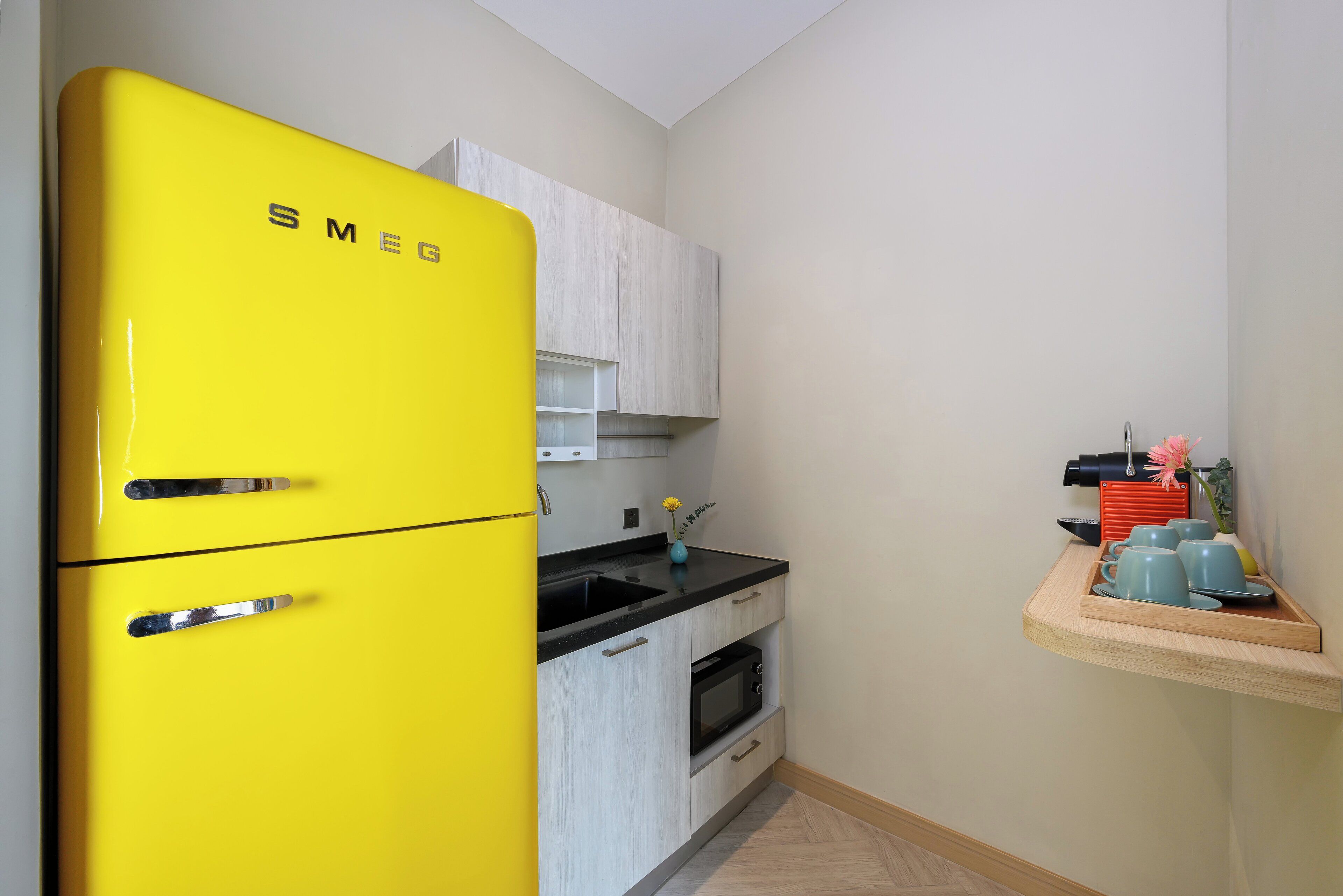 A compact kitchen with a yellow refrigerator, wooden cabinets, a microwave, and a small countertop with a tray holding cups and a vase.