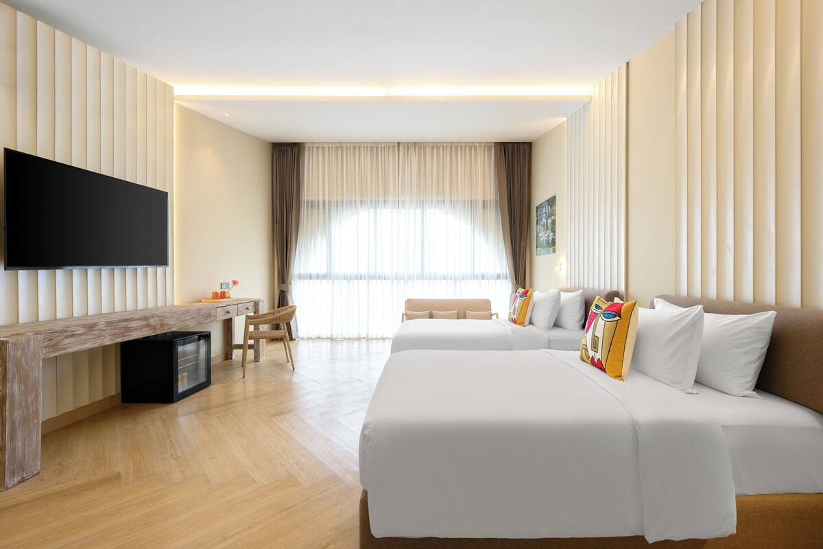 A hotel room with two beds, a desk, a chair, and a TV.