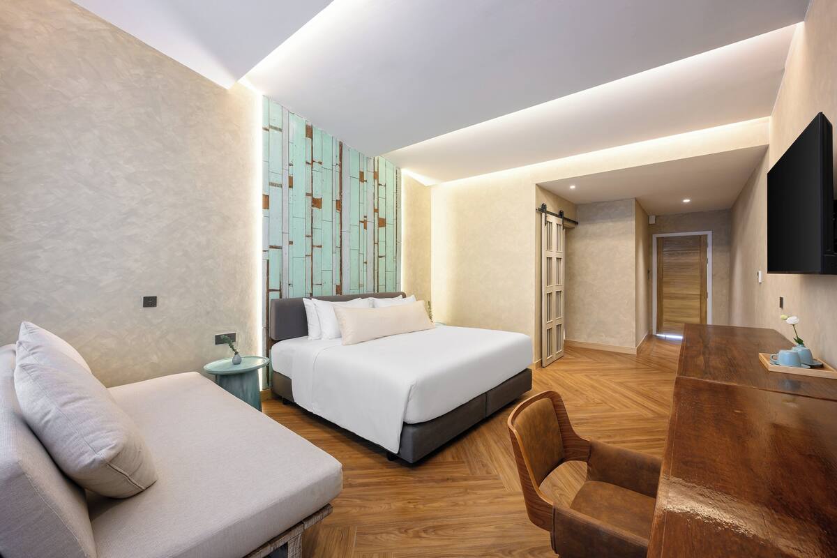 A modern hotel room with a bed, a sofa, a wooden desk, and a TV.