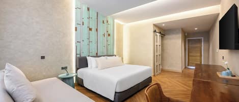 A modern hotel room with a bed, a sofa, a wooden desk, and a TV.
