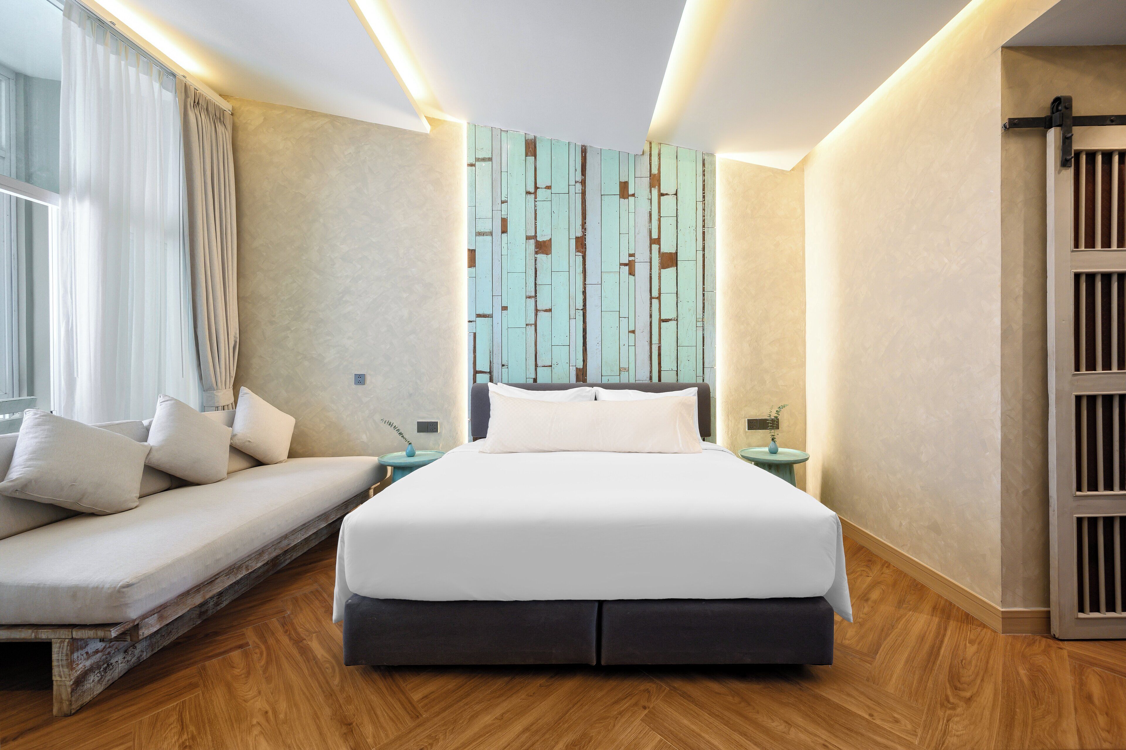 A modern hotel room with a large bed, a sofa, a nightstand, and a wall with a geometric pattern.