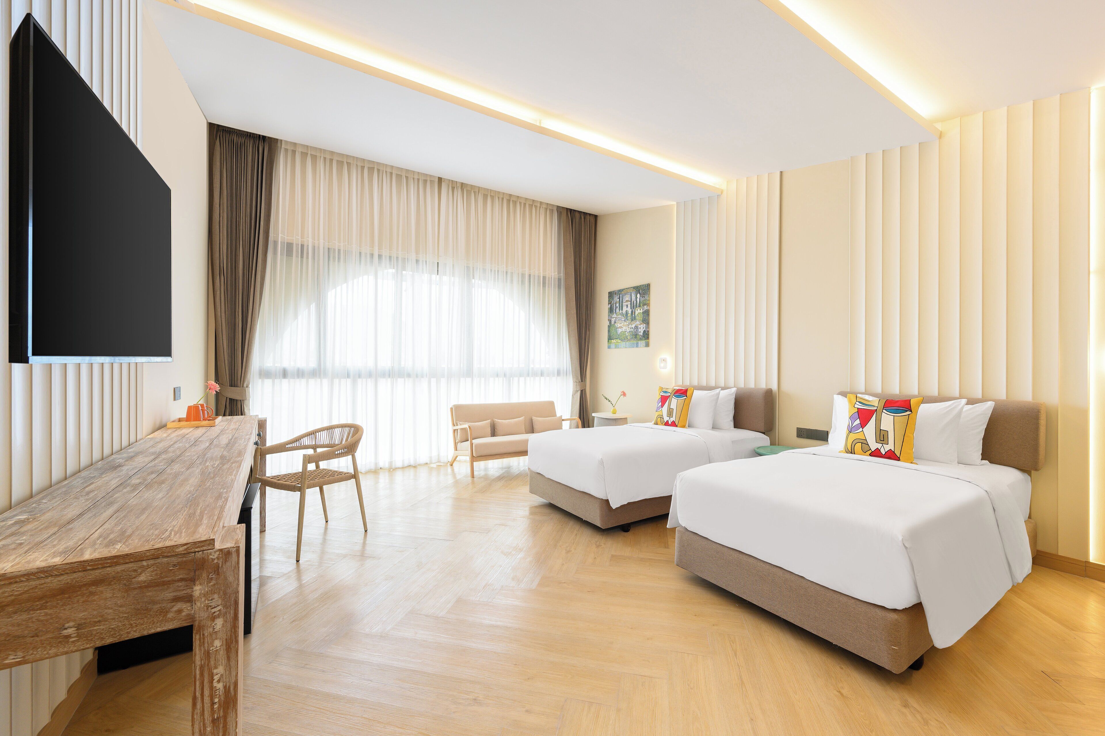 Une chambre d’hôtel avec un bureau en bois, deux lits, un canapé et une grande fenêtre avec des rideaux.