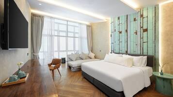 A modern hotel room with a large bed, a wooden desk, a sofa, and a TV mounted on the wall.