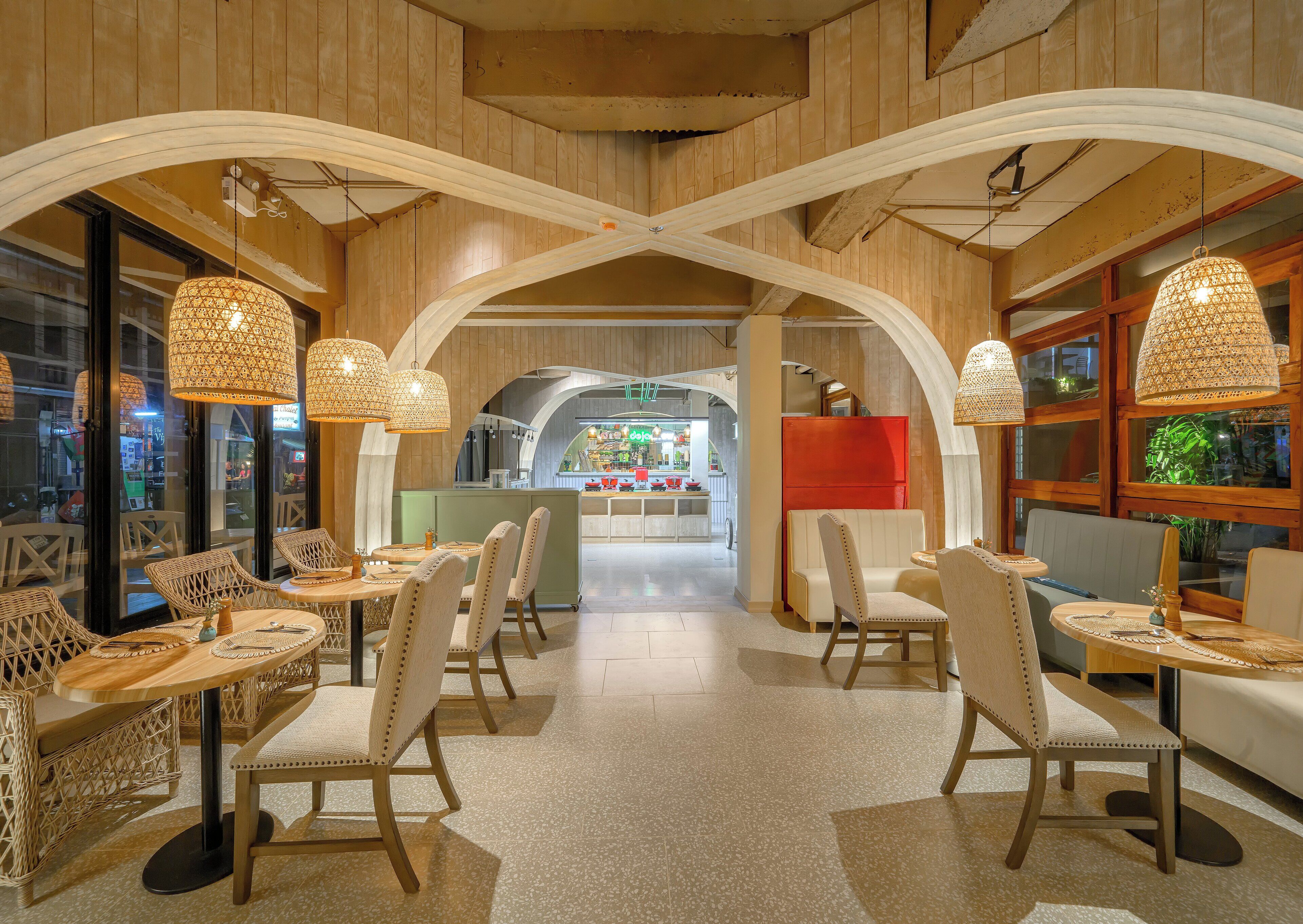 A restaurant with high wooden ceilings, wicker furniture, and hanging lamps.