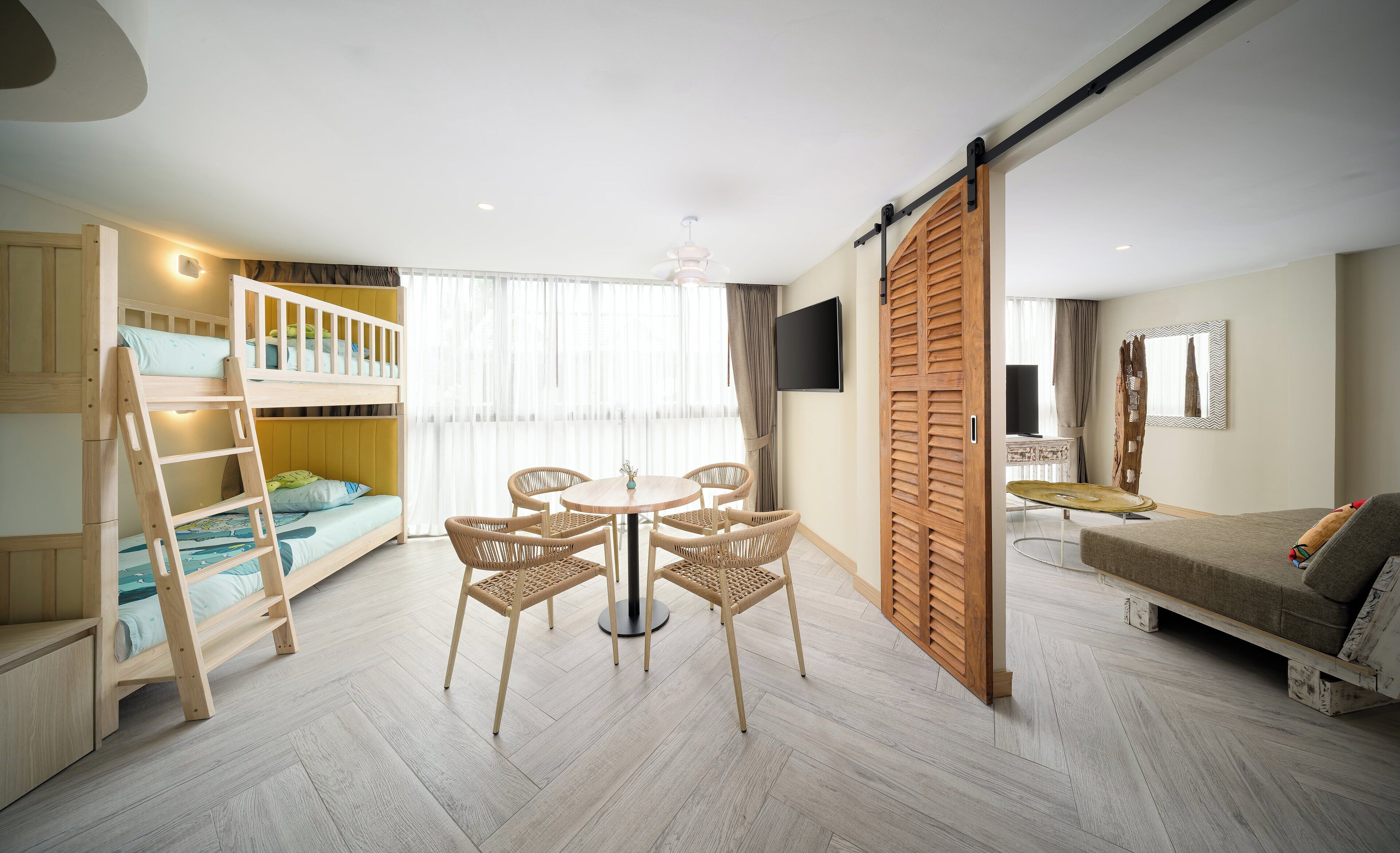 A modern, well-lit room with a bunk bed, a dining table with chairs, a sofa, and a TV mounted on the wall.