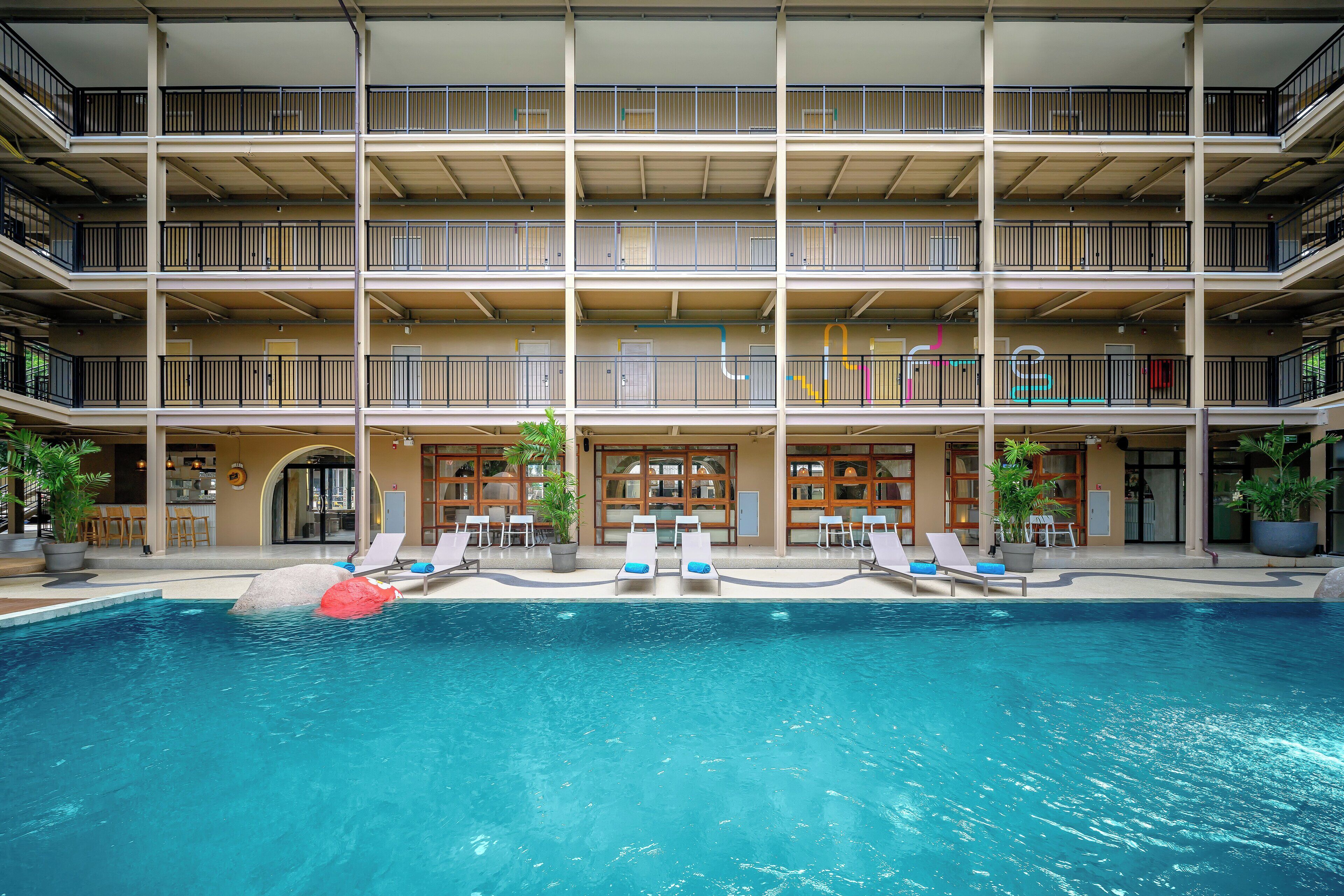 Un hôtel à plusieurs étages doté d’une piscine, de balcons et d’espaces extérieurs aménagés pour se détendre.