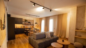 A modern living room with a sofa, a dining table, and a kitchen in the background. - Lepanto Xenia Apartments 3F (Nafpaktos)