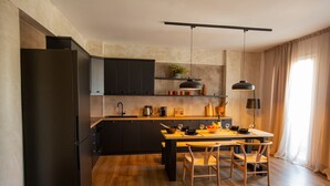 A modern kitchen with dark cabinetry, a wooden countertop, and a dining area with a table and chairs. - Lepanto Xenia Apartments 3F (Nafpaktos)