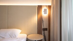 Una habitación de hotel con una cama, una mesita redonda pequeña y una lámpara de pared.