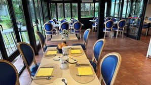 Un comedor con mesas dispuestas para cuatro, sillas tapizadas en azul y vistas al exterior a través de amplias ventanas.