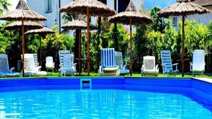 Una piscina con sillones blancos y sombrillas de paja.