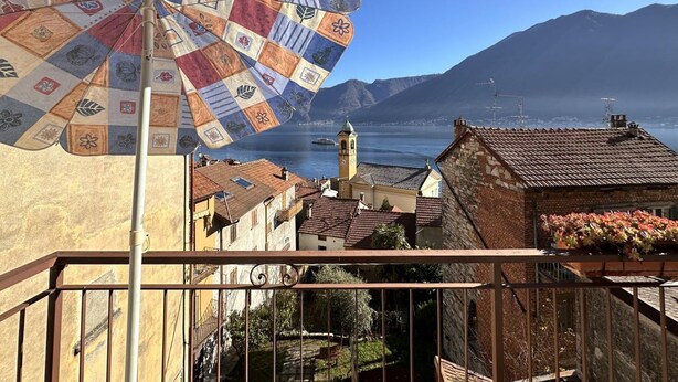 Uma varanda com vista para uma cidade costeira, um guarda-sol estampado e uma montanha ao fundo.