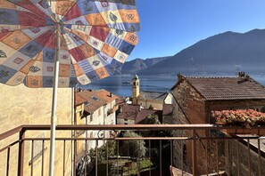Ein Balkon mit Blick auf eine Küstenstadt, einem gemusterten Sonnenschirm und einem Berg im Hintergrund.
