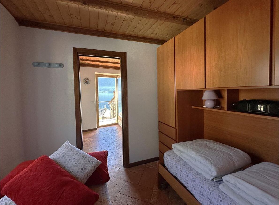 A bedroom with a wooden headboard, a bed, a red pillow, a lamp, and a view through an open door.