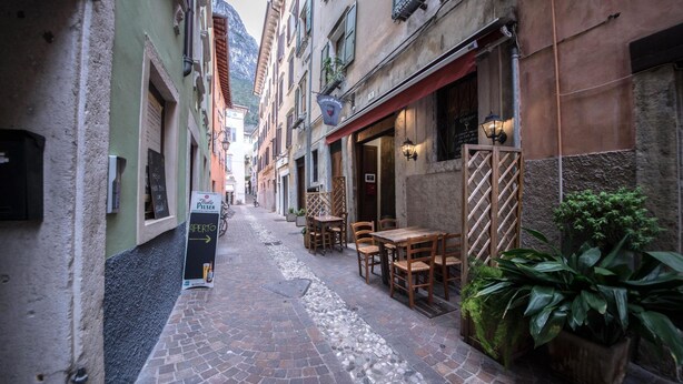 Una stretta strada acciottolata con tavoli all'aperto di un ristorante, circondata da edifici storici.