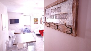 Una camera d'albergo con zona pranzo, televisore montato a parete e un cartello con su scritto 'HOME AT HOME'.