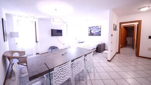 Un'area pranzo moderna con un tavolo lungo, sedie bianche e una TV a schermo piatto montata a parete.