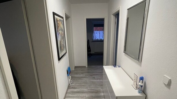 A hallway with a white reception desk, framed artwork, and a mirror on the wall. - Gemütliche 3 Zimmer Wohnung in Wolfenbüttel Linden (Wolfenbüttel)