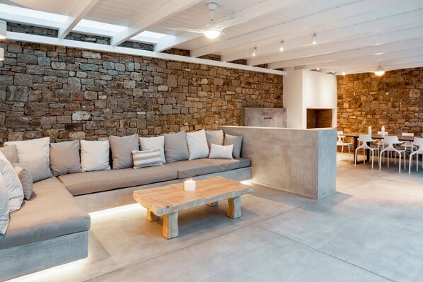 A modern living area with a stone wall, a sofa, a coffee table, and a fireplace. - Apollo Paradise Seaview Infinity Pool Jacuzzi (Mykonos)