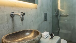 Et badeværelse med vask i sten, et spejl, en bruser og et toilet.