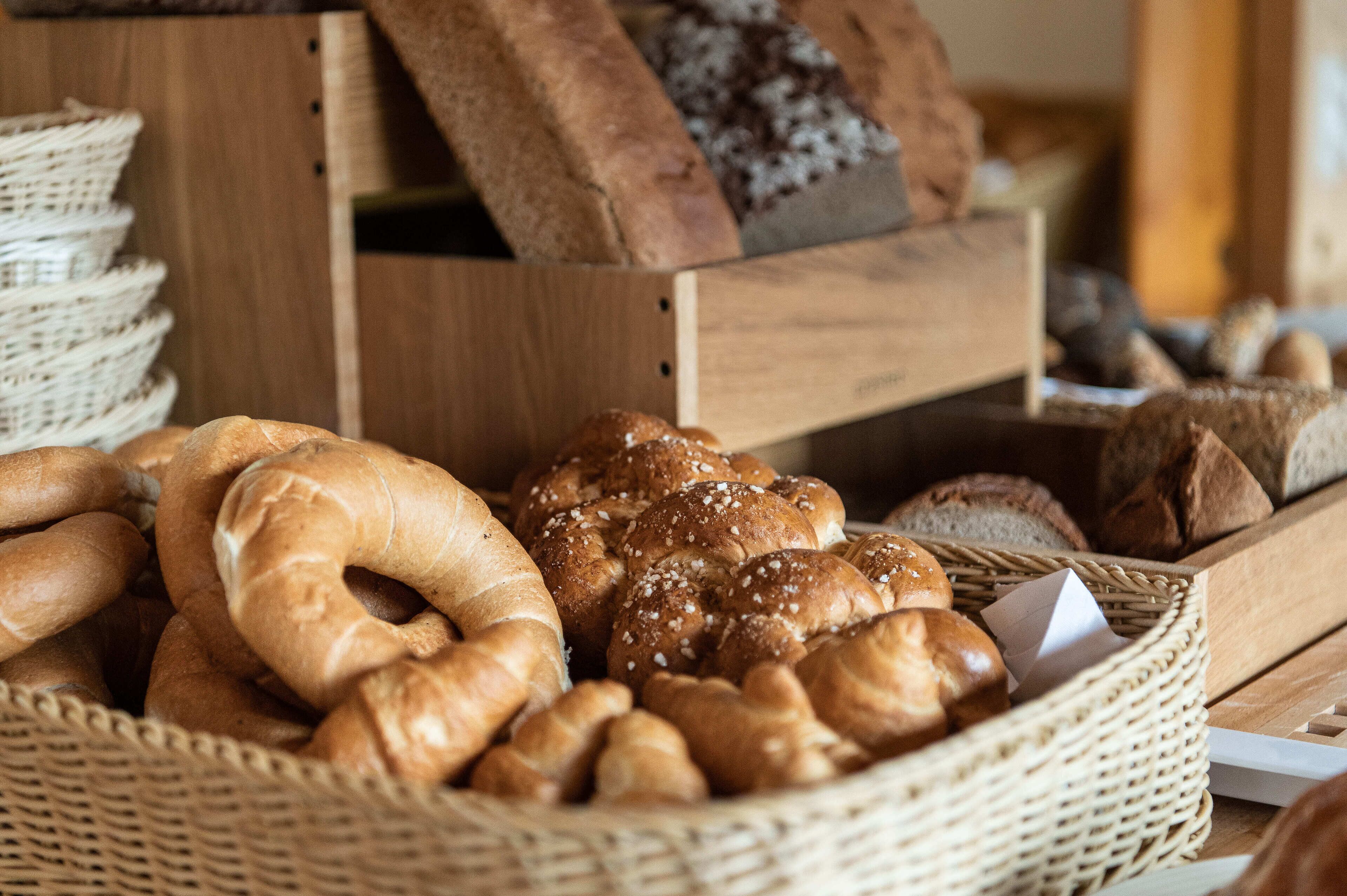 A basket filled with various types of bread, including bagels and rolls, placed on a wooden table.