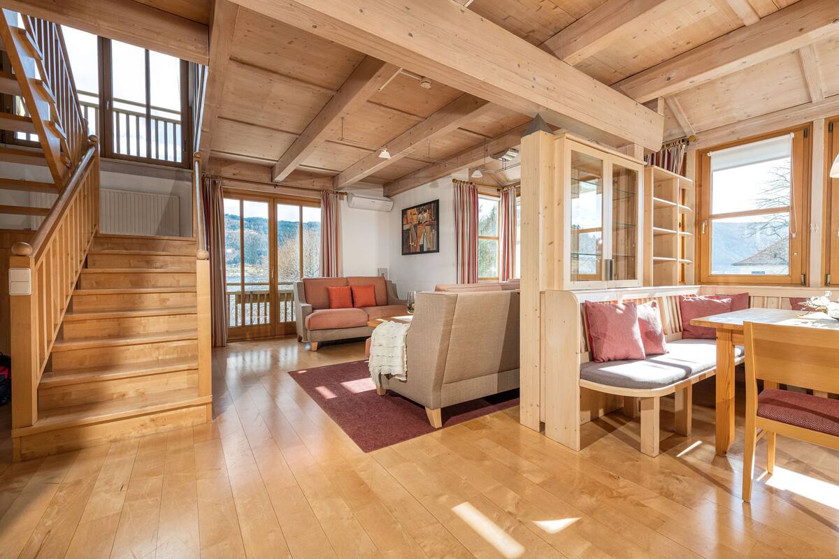 Een ruime woonkamer met een houten trap, een bank, een eettafel en een boekenkast.