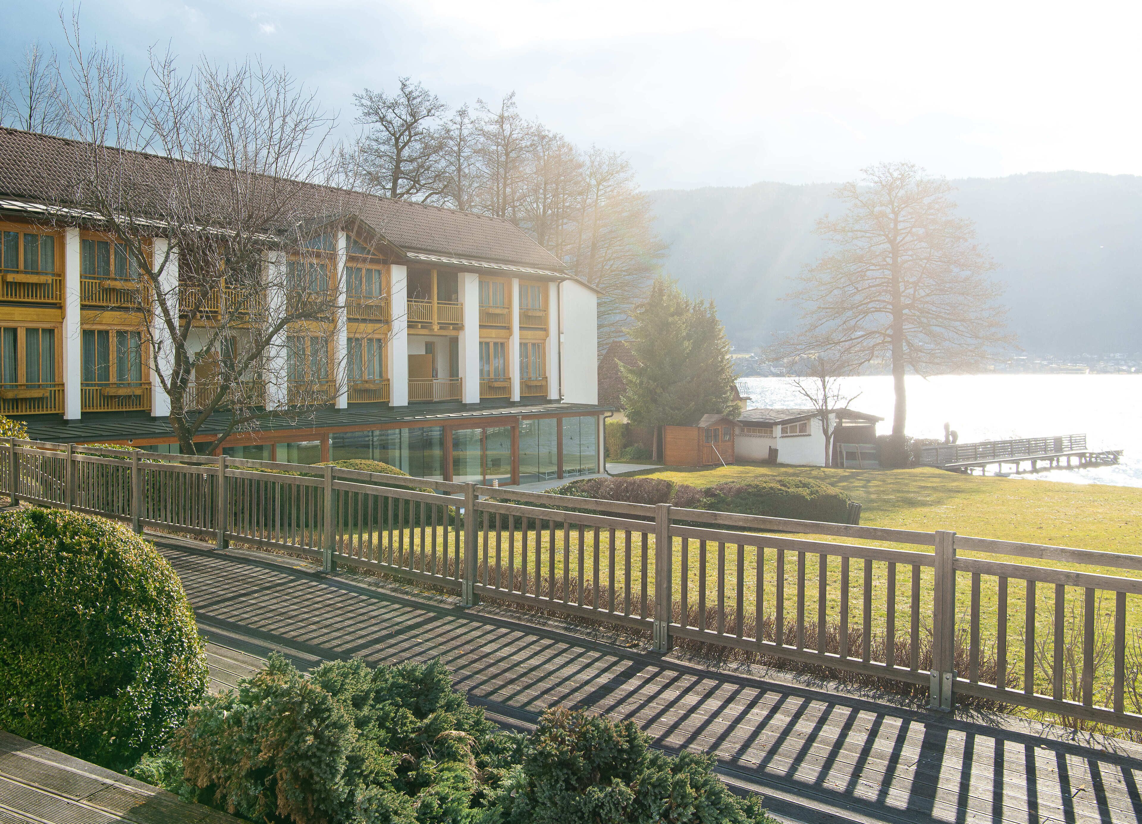 Un edificio moderno con fachada de vidrio, una terraza de madera y vistas a un lago.