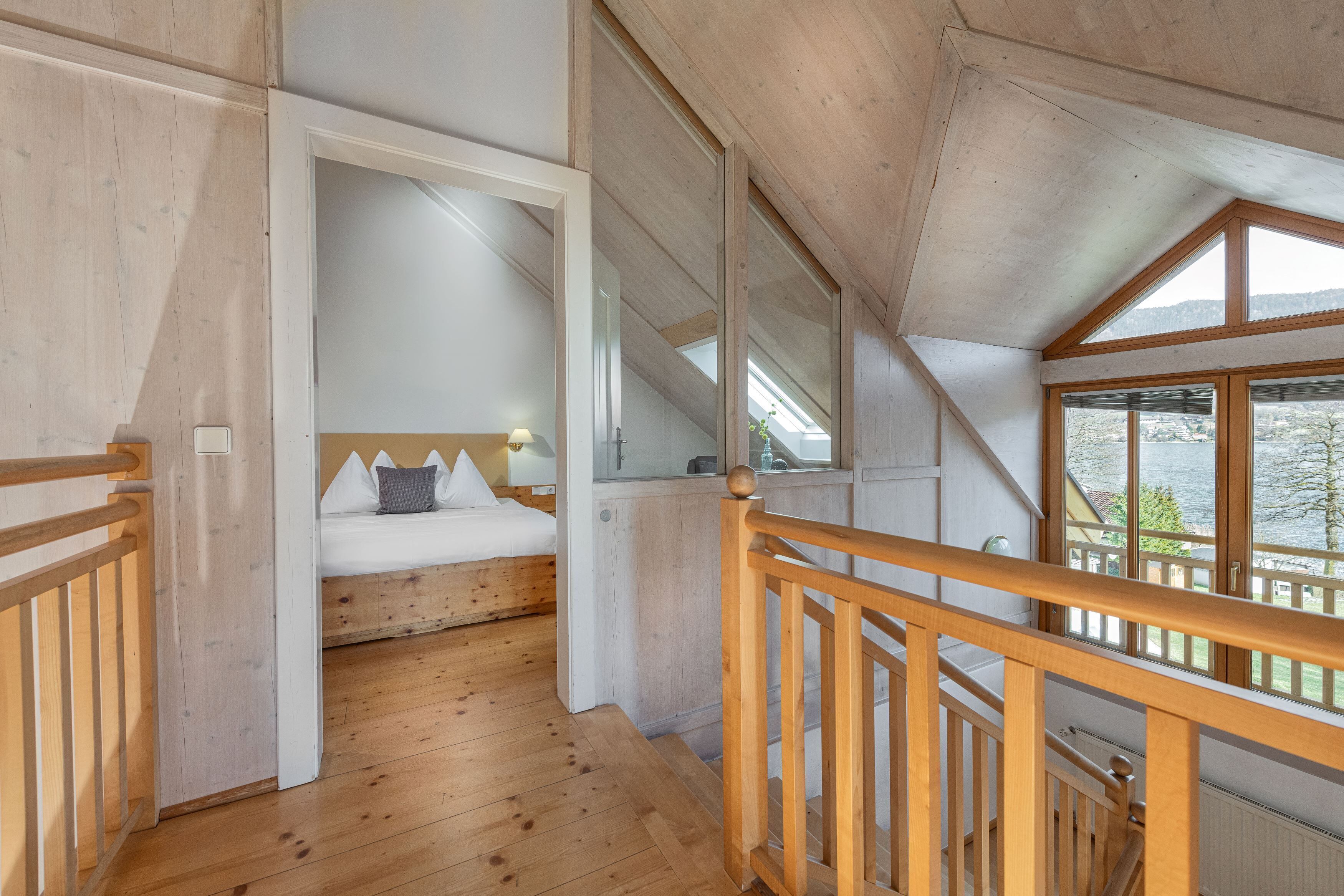 Un interior de madera con una cama, vistas al exterior y una escalera.