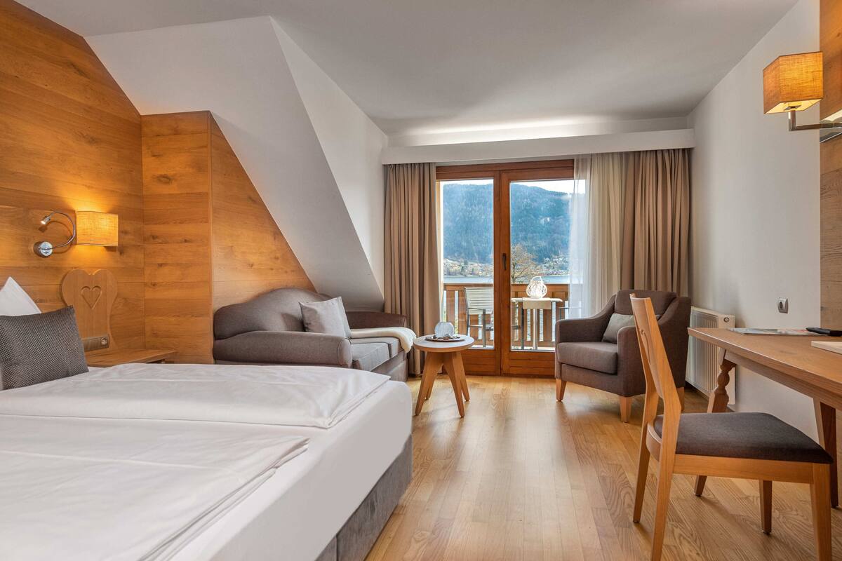Een hotelkamer met een groot bed, een bank, een eettafel en een stoel. Er is een balkon met uitzicht op de bergen.