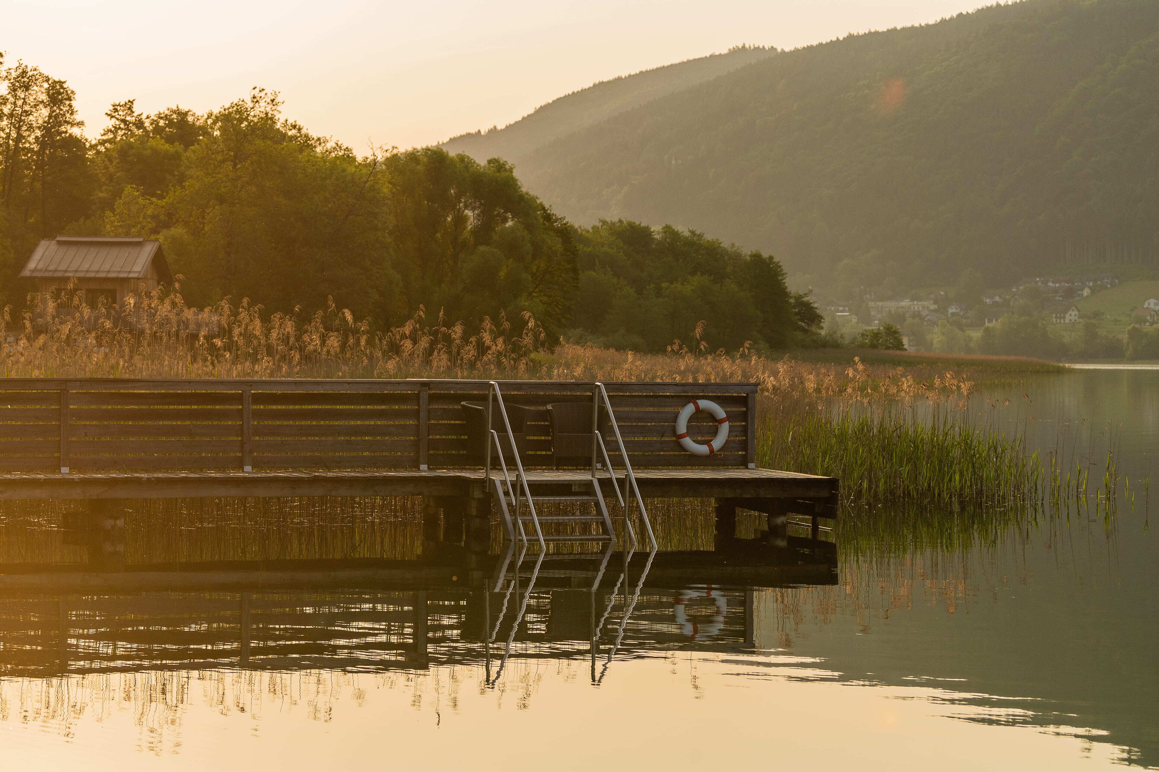 A wooden dock extending into a calm lake, surrounded by lush greenery and hills.