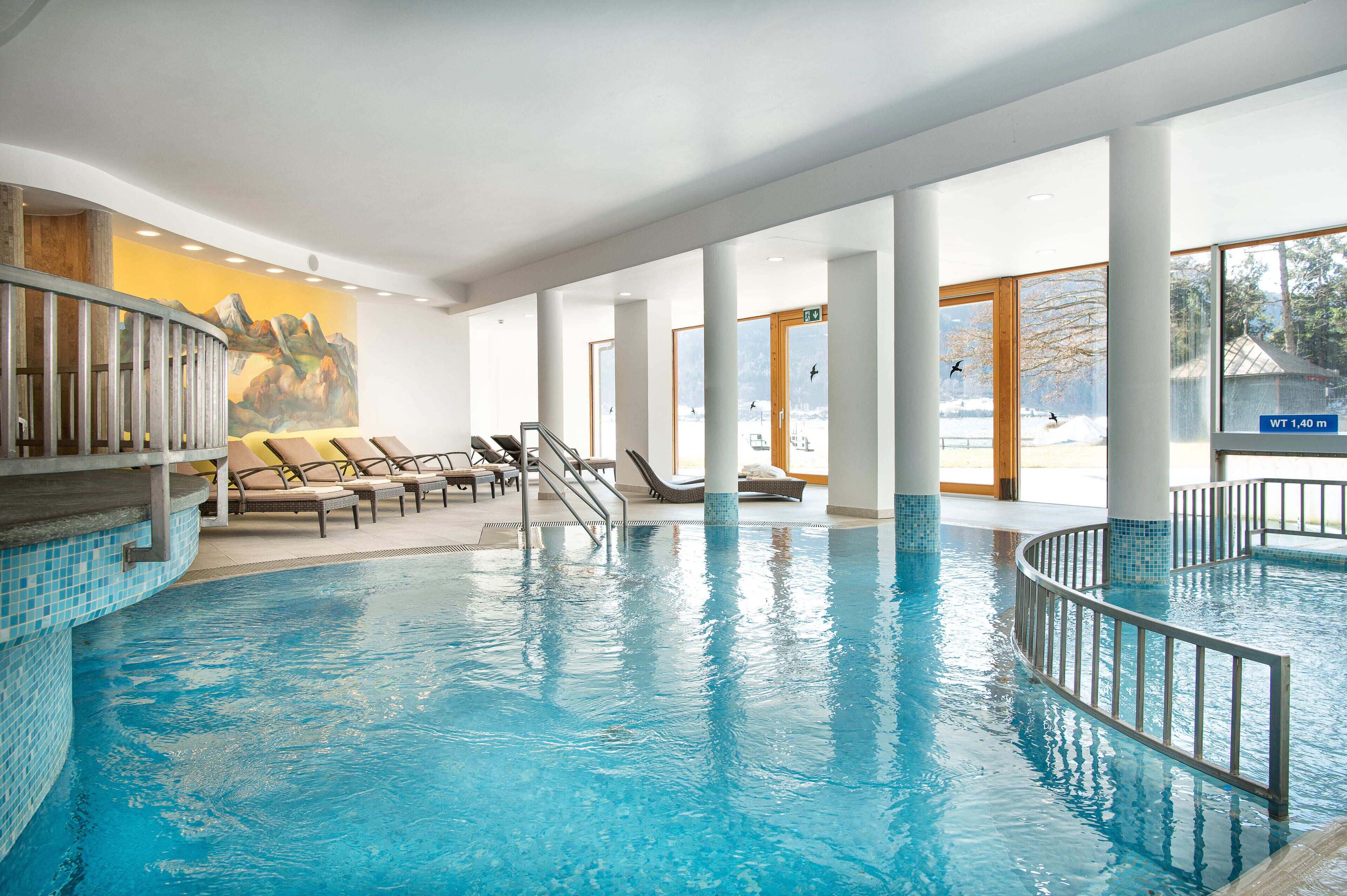 A large indoor swimming pool with a sunlit area and lounge chairs.